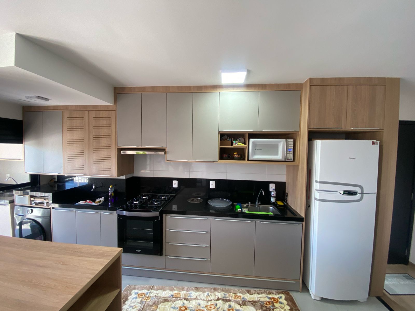 Cozinha planejada com armários em madeira e cinza, bancada preta e eletrodomésticos embutidos