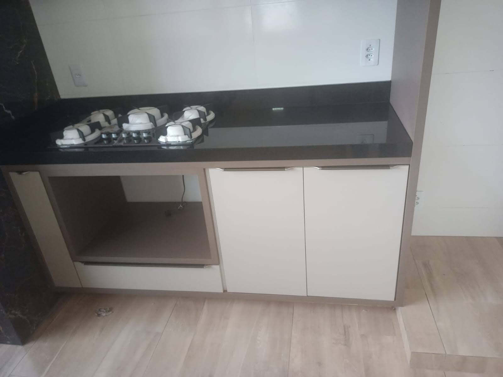Balcão planejado com cooktop, armários inferiores em tom neutro e bancada preta
