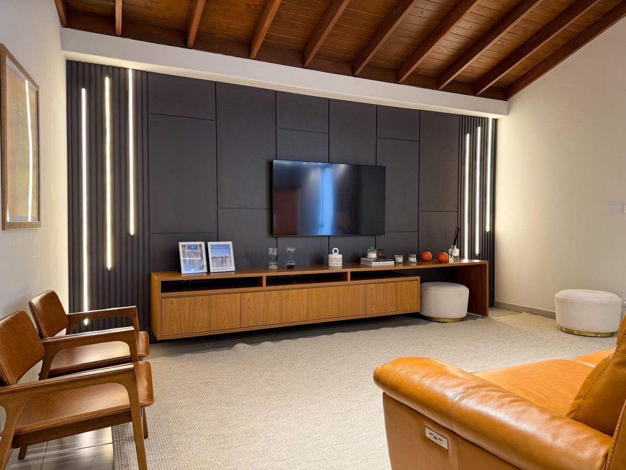 Sala de estar com painel ripado escuro, rack em madeira e iluminação vertical embutida