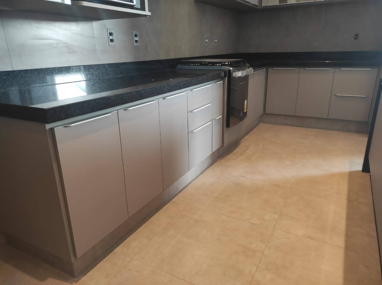 Cozinha planejada em L com bancada preta, armários inferiores e forno embutido