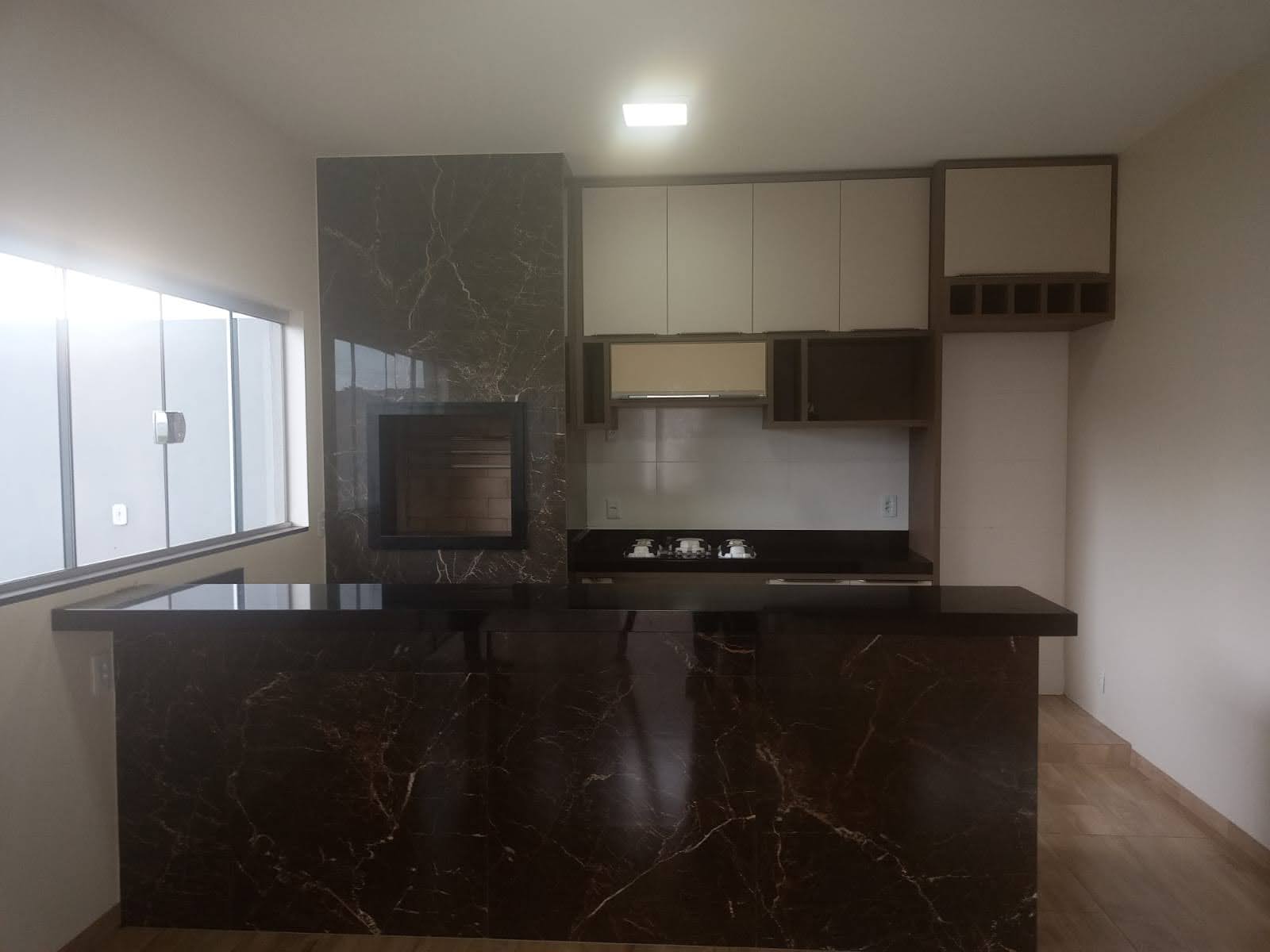 Ambiente integrado com churrasqueira, revestimento escuro, bancada e marcenaria planejada