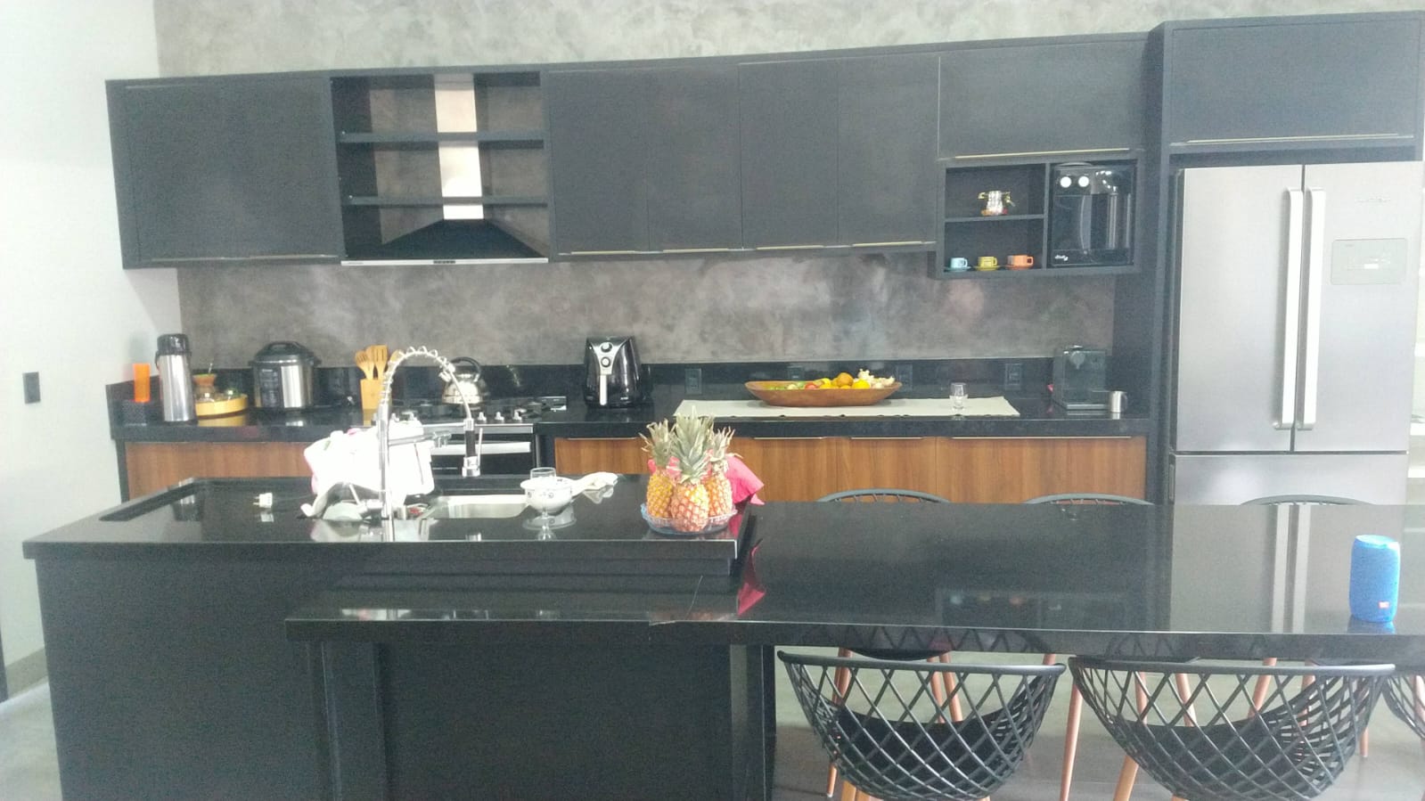 Cozinha planejada em tons escuros com ilha central, bancada preta e armários sob medida