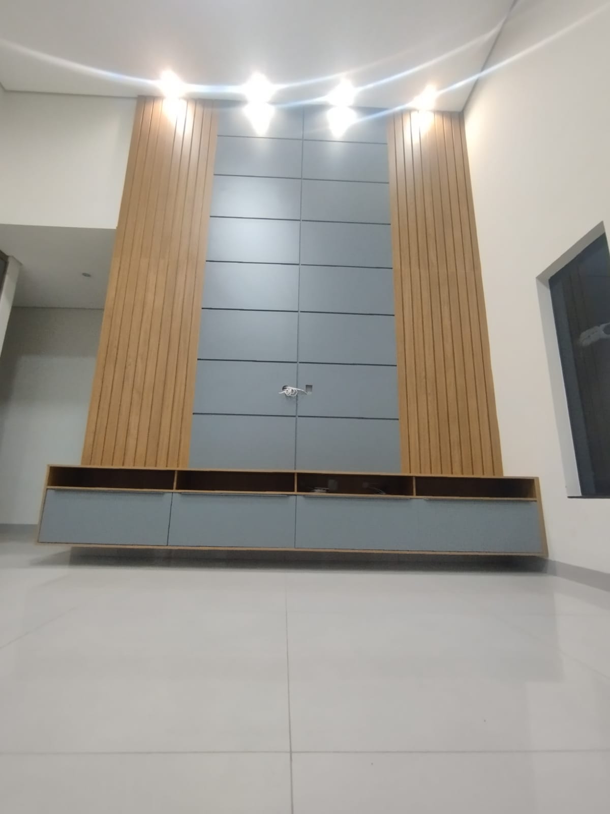 Painel para TV alto com rack suspenso, acabamento em madeira ripada e cinza, e iluminação de sanca